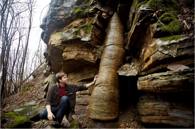 David Rives standing by a tree fossil extending through many layers of rock